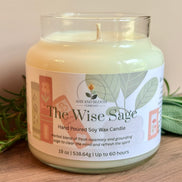 Candle labeled 'The Wise Sage' from Ash & Bloom Company on a wooden surface with greenery.