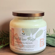 Rosemary and sage candle jar labeled 'The Wise Sage' on a wooden surface with greenery in the background