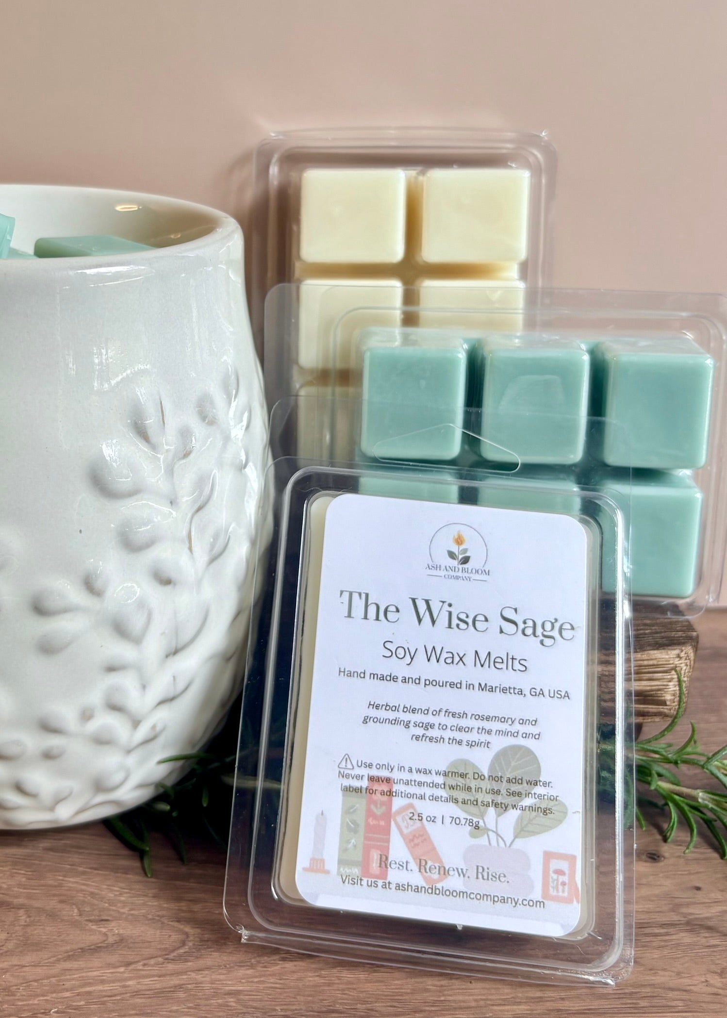Packaged rosemary and sage soy wax melts labeled 'The Wise Sage' next to a white textured wax melter on a wooden surface.