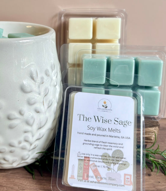 Packaged rosemary and sage soy wax melts labeled 'The Wise Sage' next to a white textured wax melter on a wooden surface.