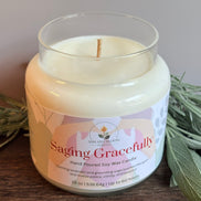 Candle in a glass jar with a label reading 'Saging Gracefully' on a wooden surface with sage leaves.