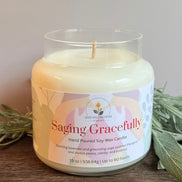 Scented candle labeled 'Saging Gracefully' with sage leaves on a wooden surface.