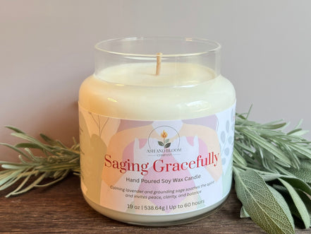 Scented candle labeled 'Saging Gracefully' with sage leaves on a wooden surface.