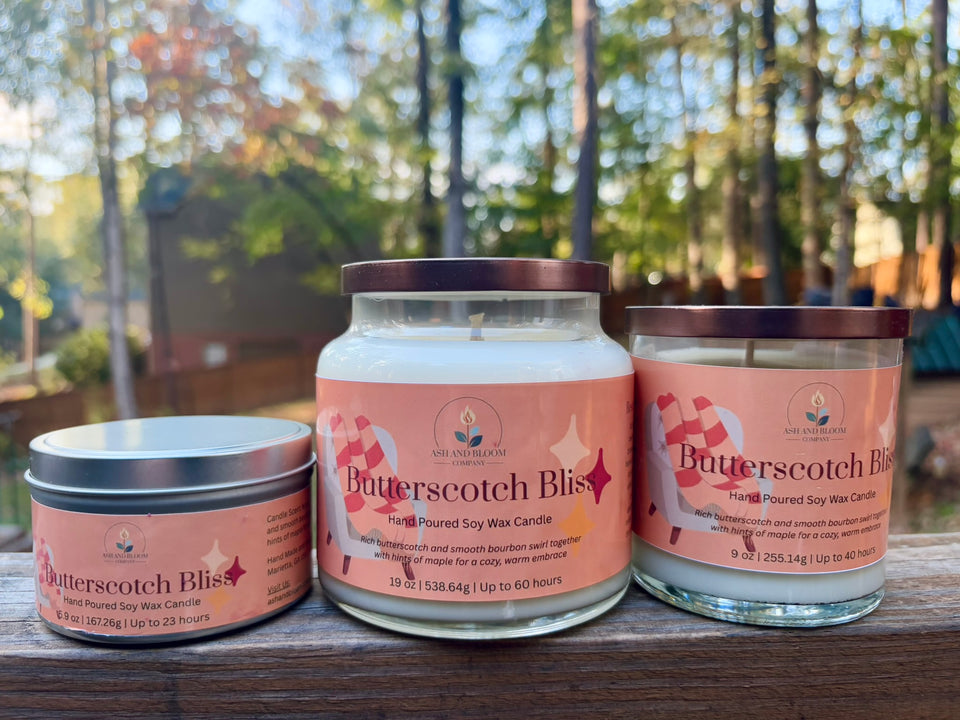 Three 'Butterscotch Bliss' butterscotch and bourbon candles on a wooden surface with a blurred outdoor background