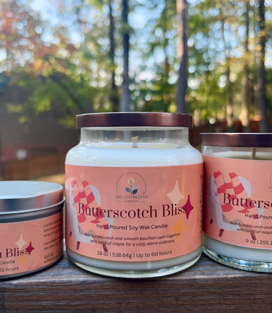 Three 'Butterscotch Bliss' butterscotch and bourbon candles on a wooden surface with a blurred outdoor background