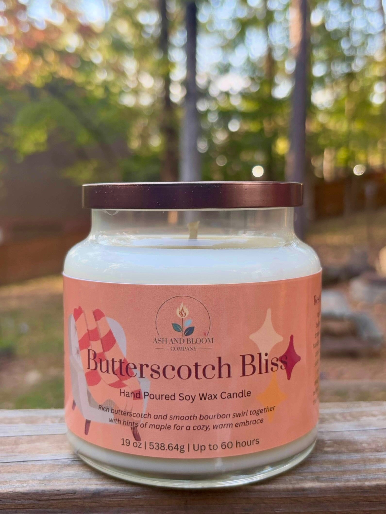 Butterscotch Bliss candle in a glass jar with a pink label outdoors.