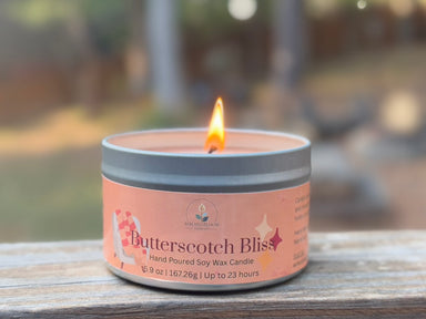 Candle labeled 'Butterscotch Bliss' on a wooden surface with a blurred outdoor background