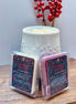 Two cranberry and apple wax melts in packaging with 'Holiday Hearth' label on a wooden surface in front of a wax warmer
