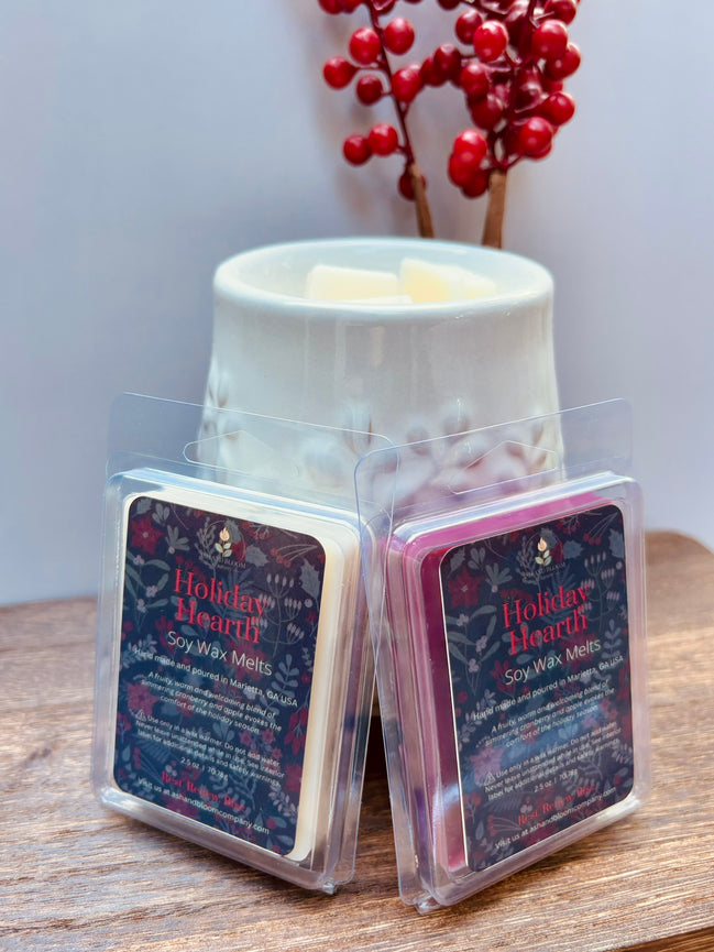 Two cranberry and apple wax melts in packaging with 'Holiday Hearth' label on a wooden surface in front of a wax warmer