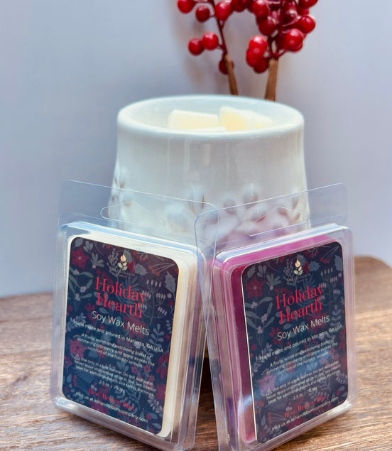 Two cranberry and apple wax melts in packaging with 'Holiday Hearth' label on a wooden surface in front of a wax warmer