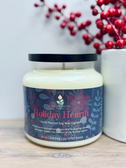 Candle jar labeled 'Holiday Hearth' with decorative berries in the background