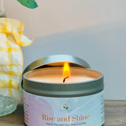 Citrus and mint candle in a tin labeled 'Rise and Shine' on a wooden surface with a blurred background