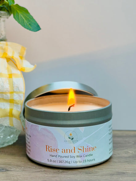 Citrus and mint candle in a tin labeled 'Rise and Shine' on a wooden surface with a blurred background