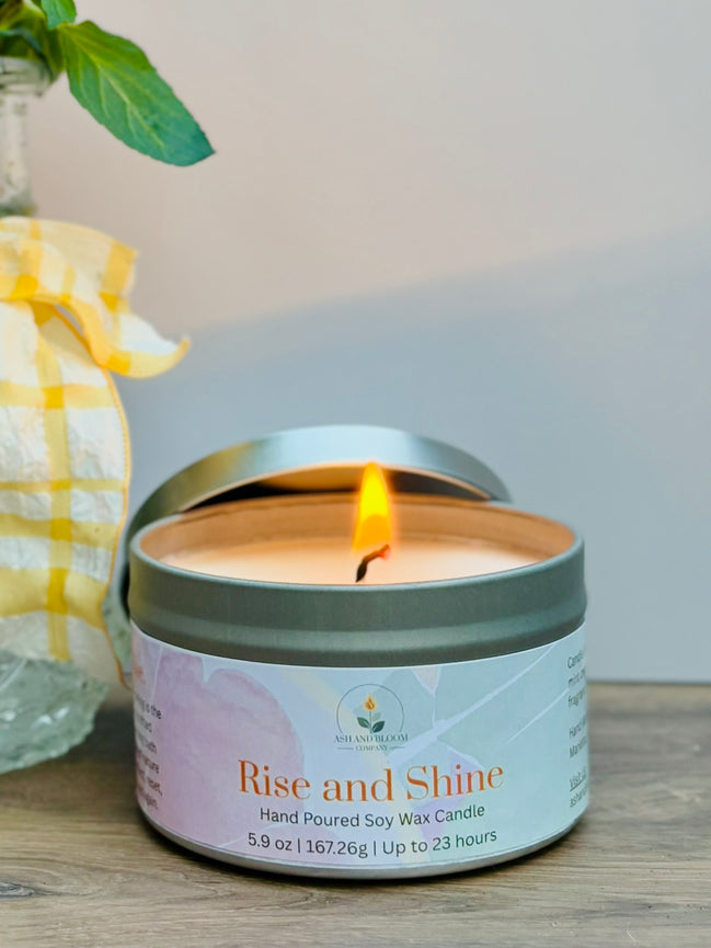 Citrus and mint candle in a tin labeled 'Rise and Shine' on a wooden surface with a blurred background