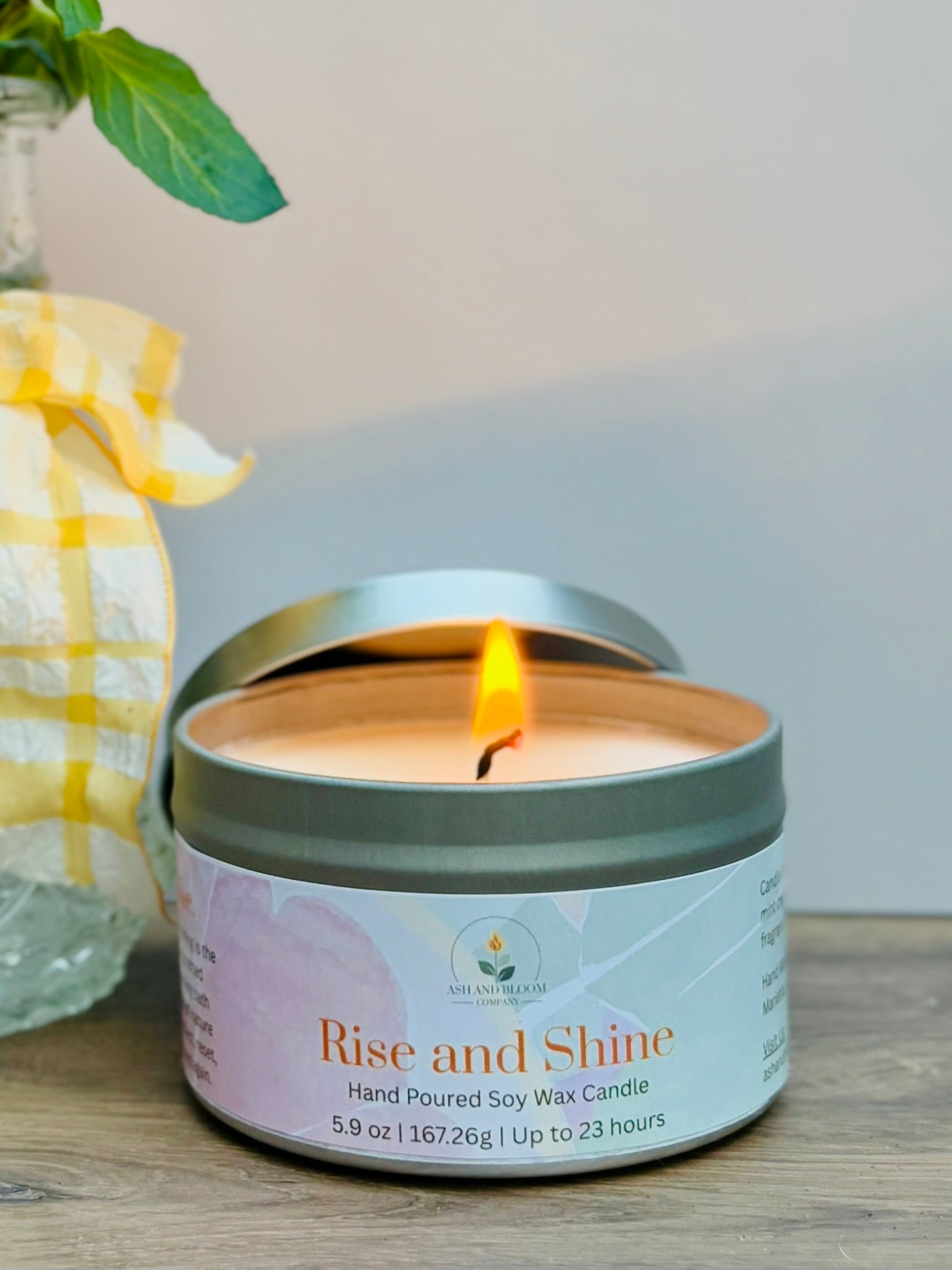 Citrus and mint candle in a tin labeled 'Rise and Shine' on a wooden surface with a blurred background