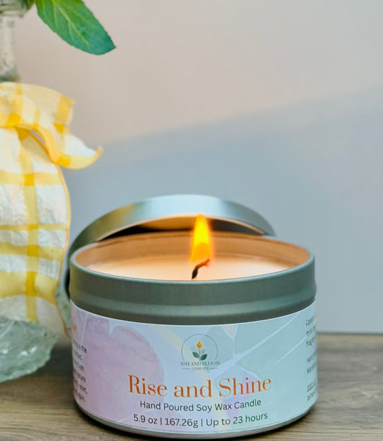 Citrus and mint candle in a tin labeled 'Rise and Shine' on a wooden surface with a blurred background