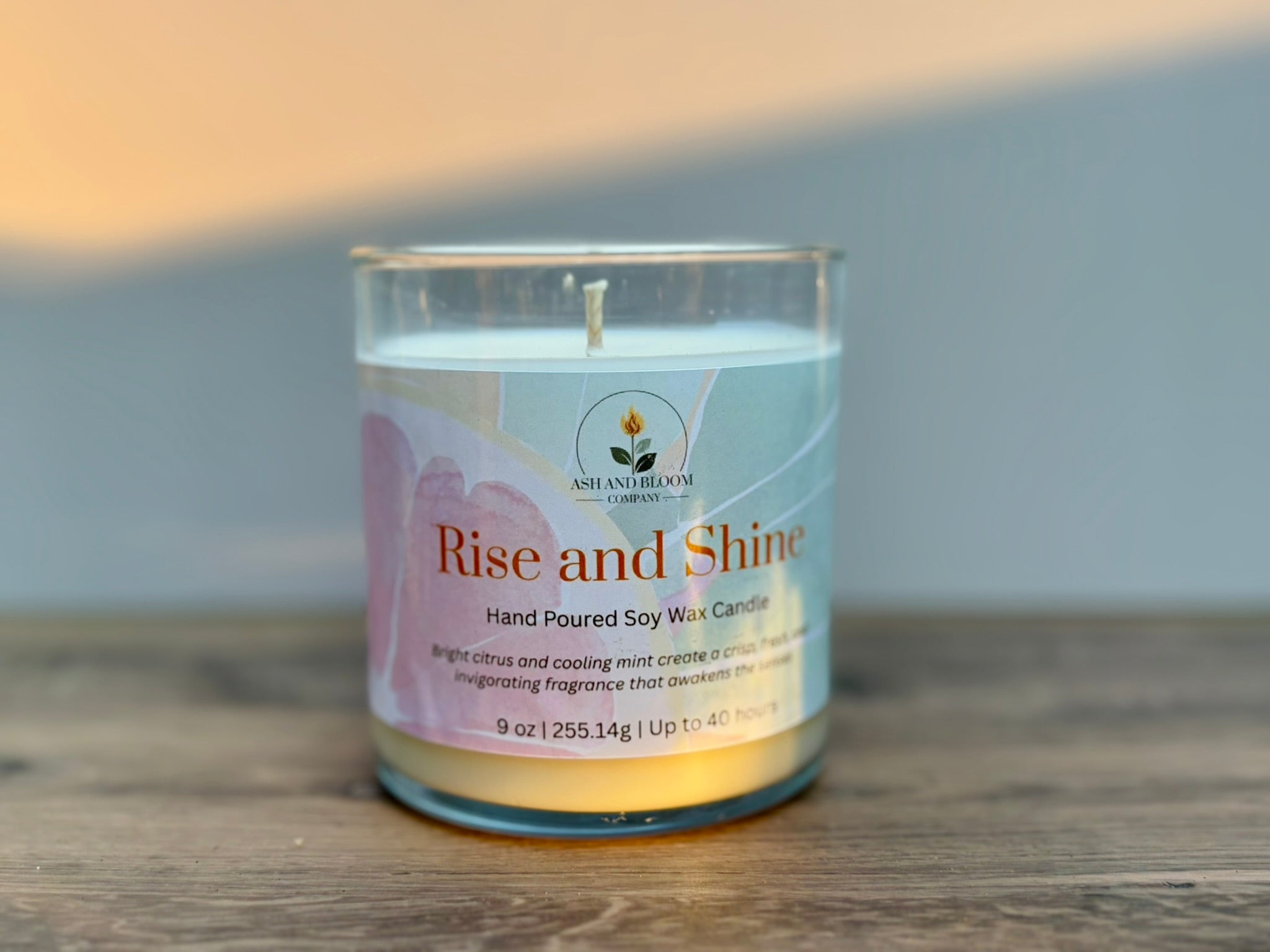 Citrus and mint candle labeled 'Rise and Shine' on a wooden surface with a neutral background