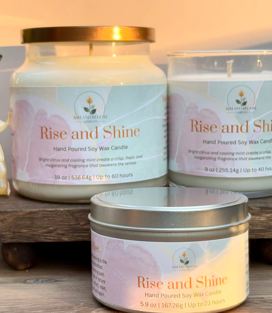 Three 'Rise and Shine' citrus and mint candles on a wooden stand with a soft background