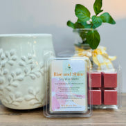 Pack of 'Rise and Shine' citrus and mint soy wax melts next to a textured ceramic wax melt container on a wooden surface.