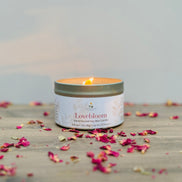 Lovebloom candle in a tin with scattered dried flowers on a wooden surface.