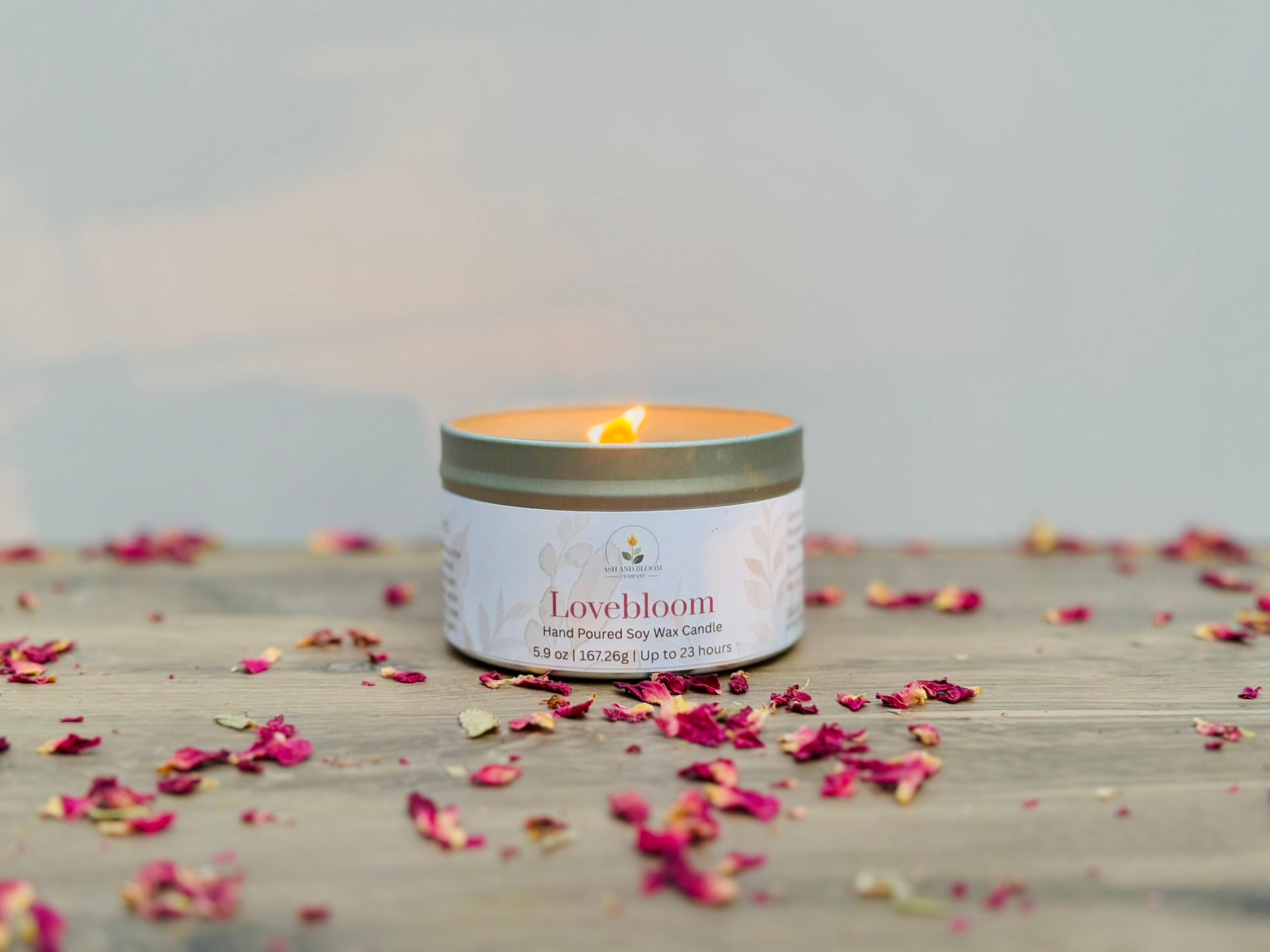 Lovebloom candle in a tin with scattered dried flowers on a wooden surface.