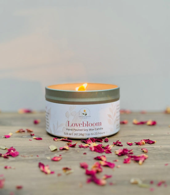 Lovebloom candle in a tin with scattered dried flowers on a wooden surface.