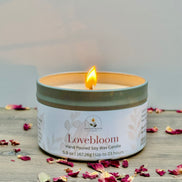 Lovebloom candle with a lit wick on a wooden surface with dried flowers.
