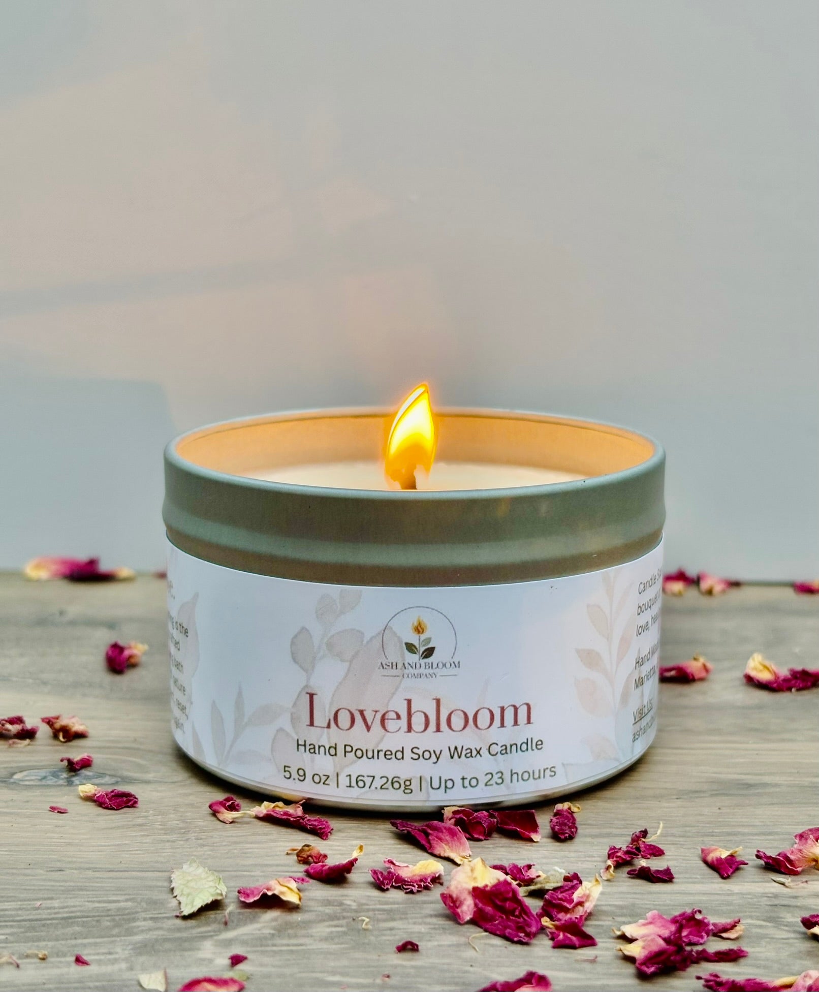 Lovebloom candle with a lit wick on a wooden surface with dried flowers.