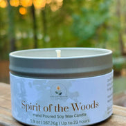 Candle in a tin labeled 'Spirit of the Woods' on a wooden surface with a blurred natural background