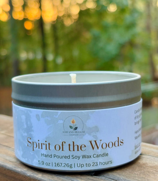 Candle in a tin labeled 'Spirit of the Woods' on a wooden surface with a blurred natural background