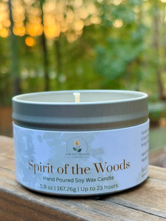 Candle in a tin labeled 'Spirit of the Woods' on a wooden surface with a blurred natural background