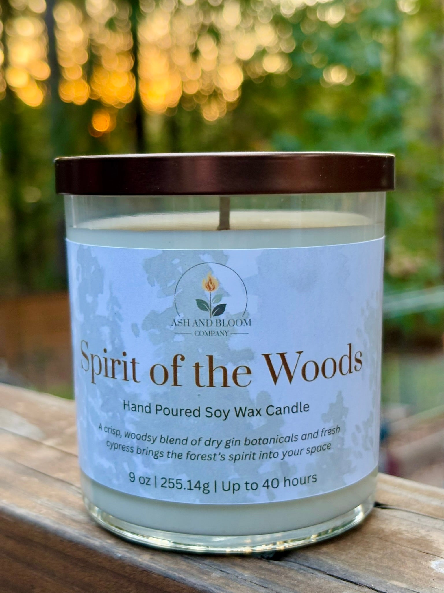 Candle labeled 'Spirit of the Woods' on a wooden surface with a blurred natural background