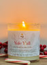 Candle labeled 'Yule Y'all' with candy canes and holly berries on a wooden surface.