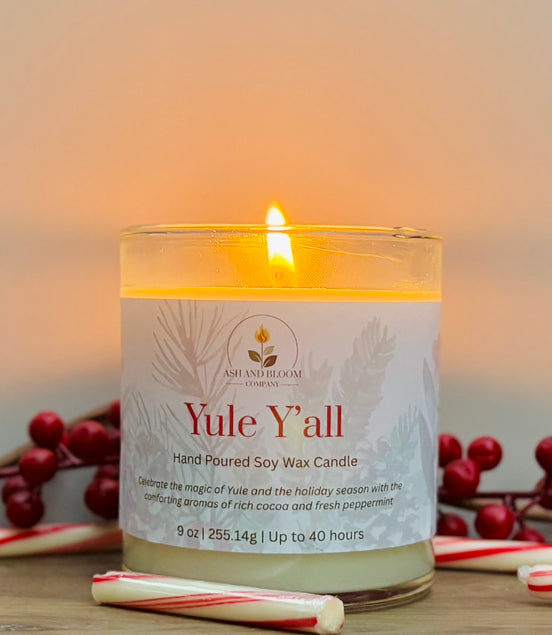 Candle labeled 'Yule Y'all' with candy canes and holly berries on a wooden surface.