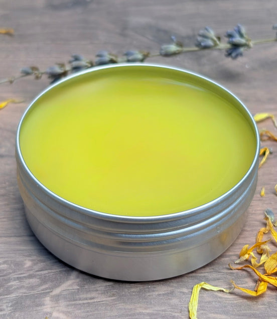 Metal tin with greenish-yellow salve on a wooden surface with dried flowers.