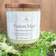 Candle labeled 'Forest Magic' on a bed of green moss with a blurred wooden background