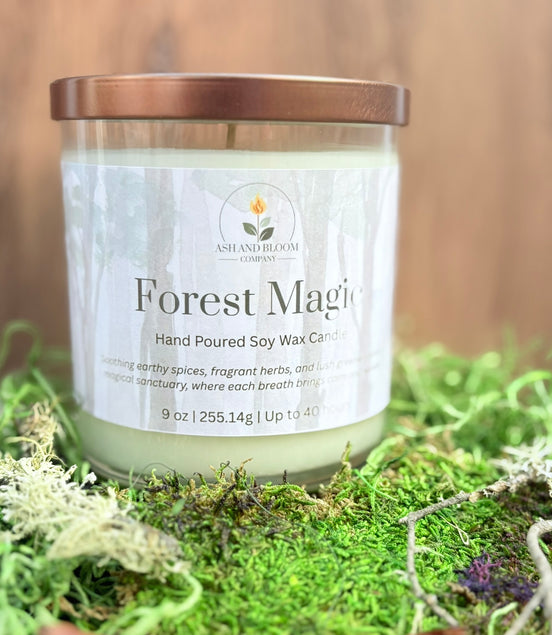 Candle labeled 'Forest Magic' on a bed of green moss with a blurred wooden background
