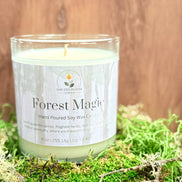 Candle labeled 'Forest Magic' on a bed of green moss with a wooden background