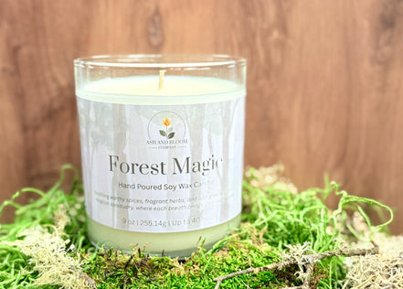 Candle labeled 'Forest Magic' on a bed of green moss with a wooden background