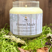 Candle labeled 'Forest Magic' on a bed of green moss with a wooden background