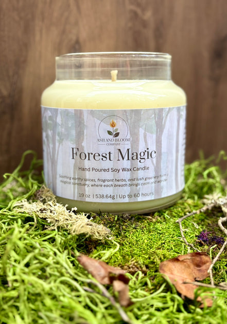 Candle labeled 'Forest Magic' on a bed of green moss with a wooden background