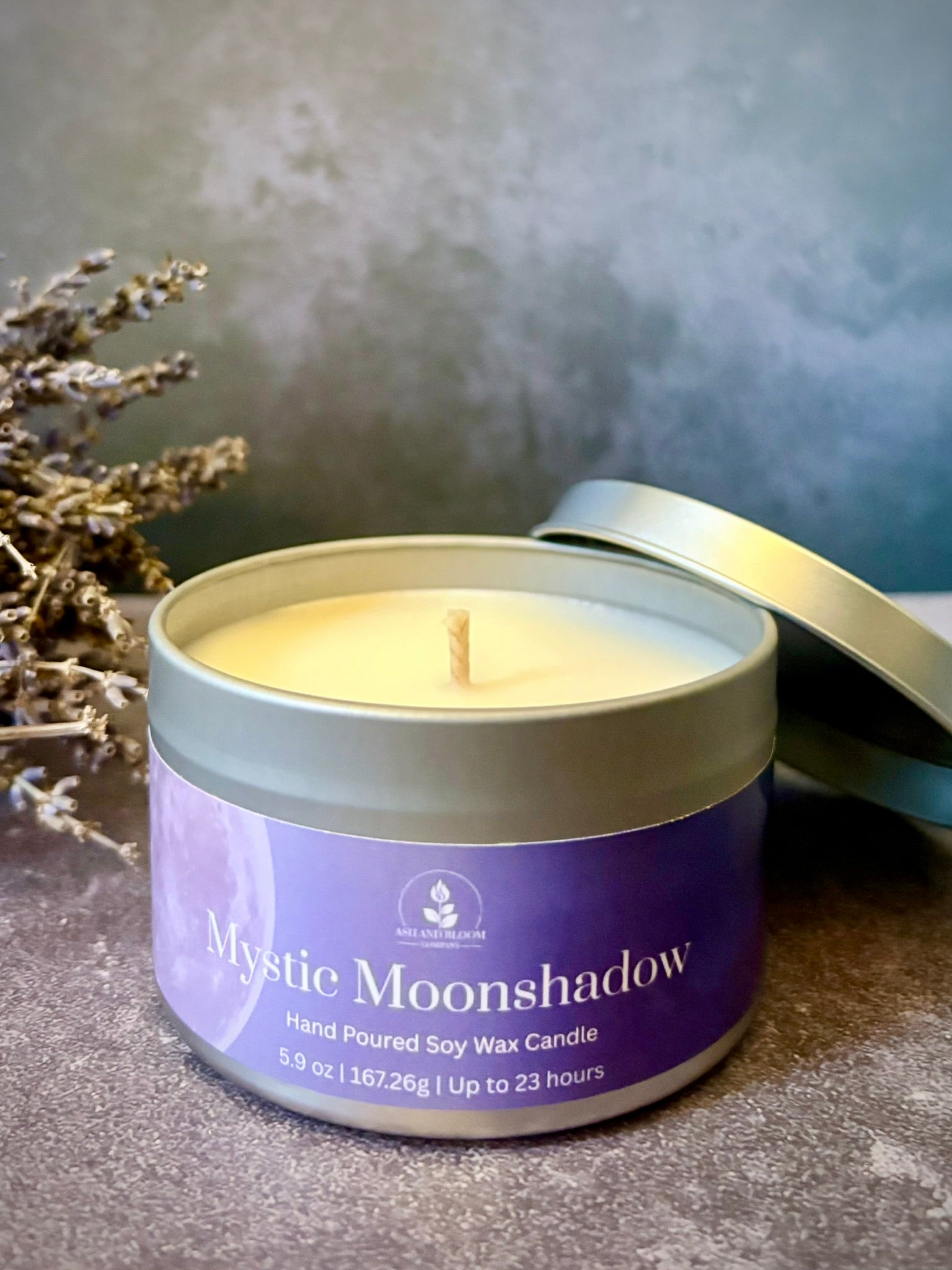 Mystic Moonshadow candle in a tin with lavender branches on a textured surface