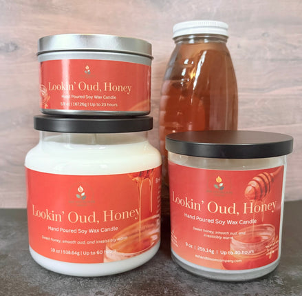 Three 'Lookin' Oud, Honey' candles of different sizes on a wooden surface with a bottle of honey in the background