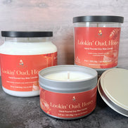 Three 'Lookin' Oud Honey' container candles with an orange label on a wood background