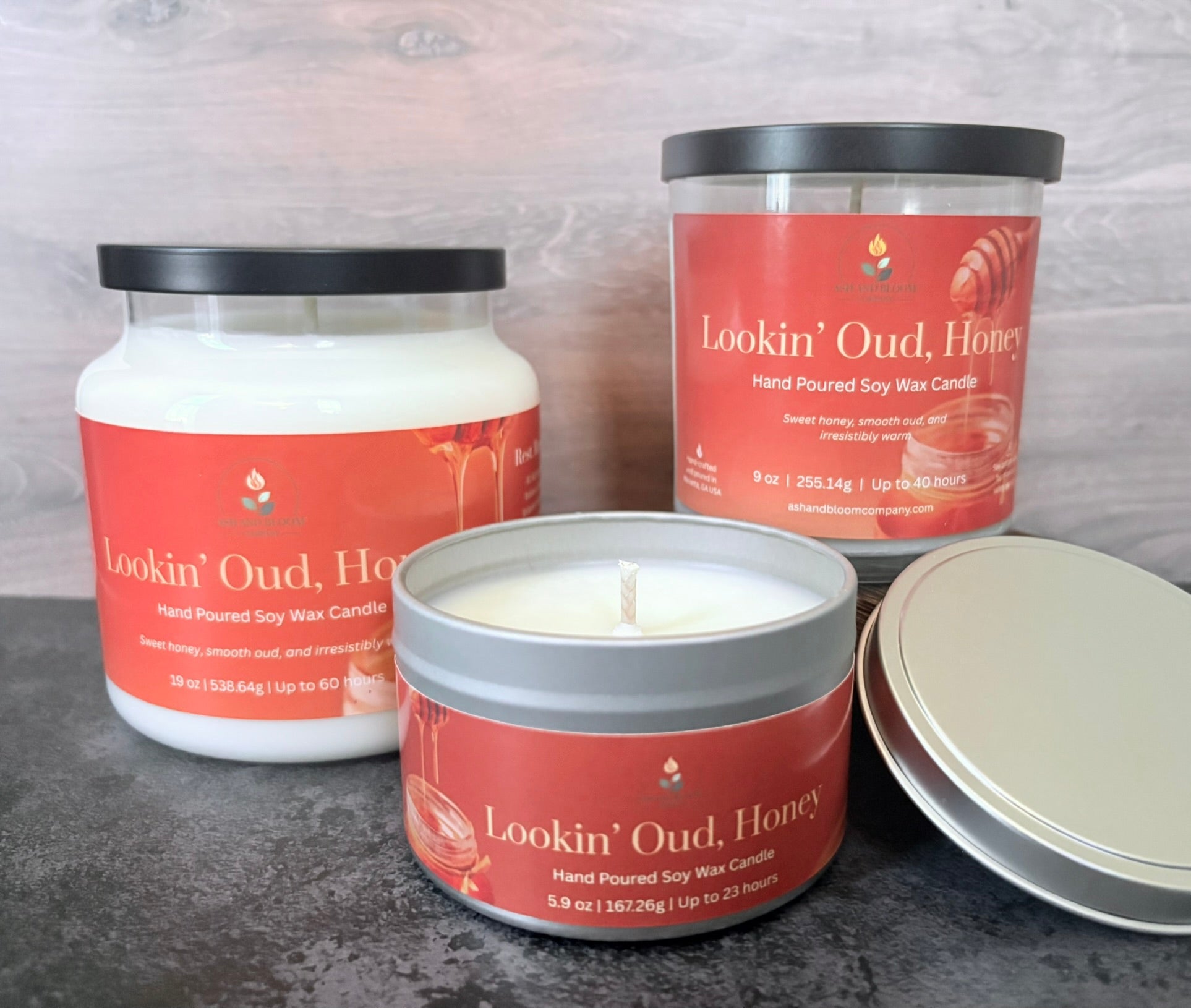 Three 'Lookin' Oud Honey' container candles with an orange label on a wood background