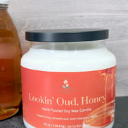 Jar of 'Lookin' Oud, Honey' candle with an orange label on a gray surface.