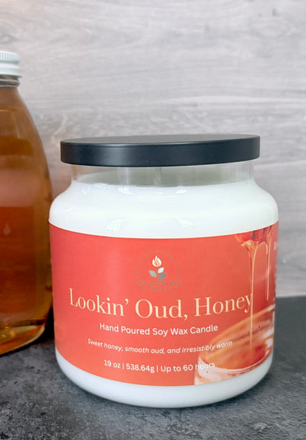 Jar of 'Lookin' Oud, Honey' candle with an orange label on a gray surface.