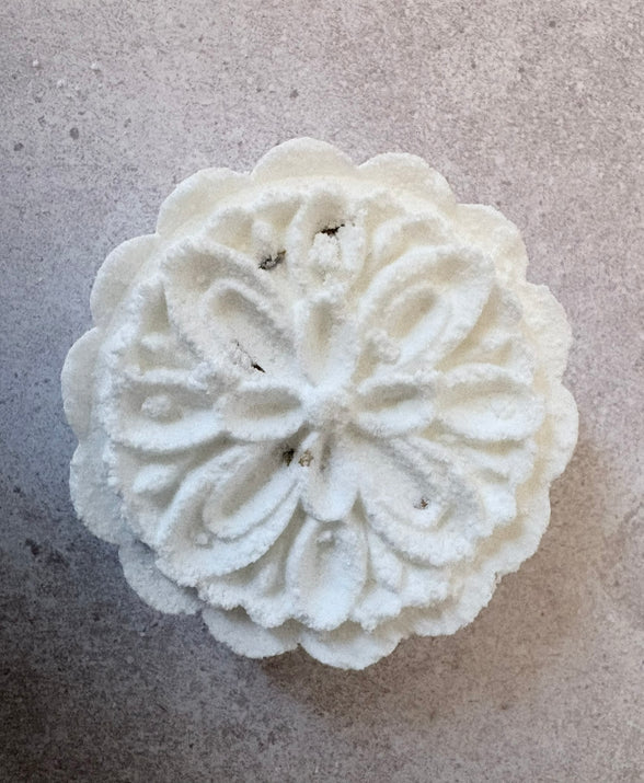 White decorative shower steamer with intricate patterns on a gray surface